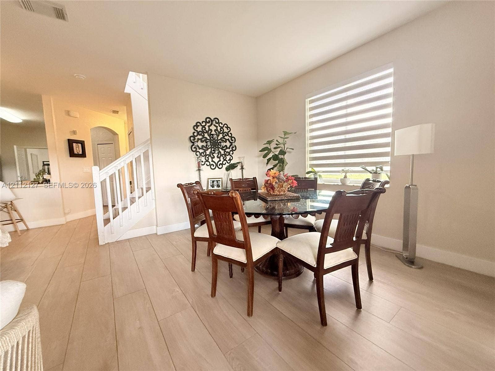 Wood-finish flooring, white staircase railing, and window treatments featuring adjustable light-filtering slats