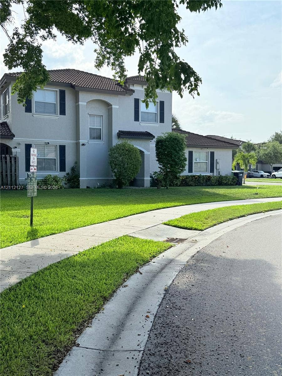 Two-story stucco exterior featuring a tile roof, decorative shutters, and arched entryway