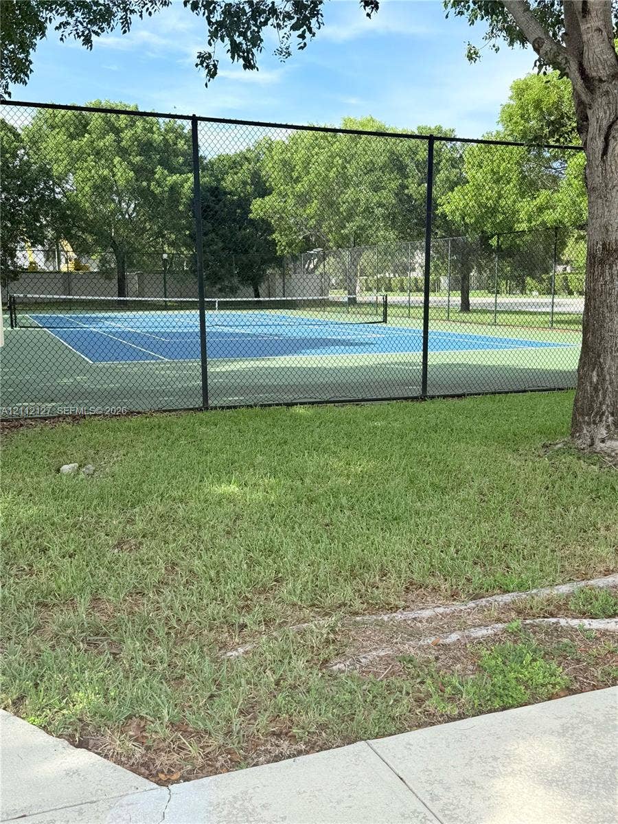 Private tennis court featuring a blue surface, mesh fencing, and a permanent net