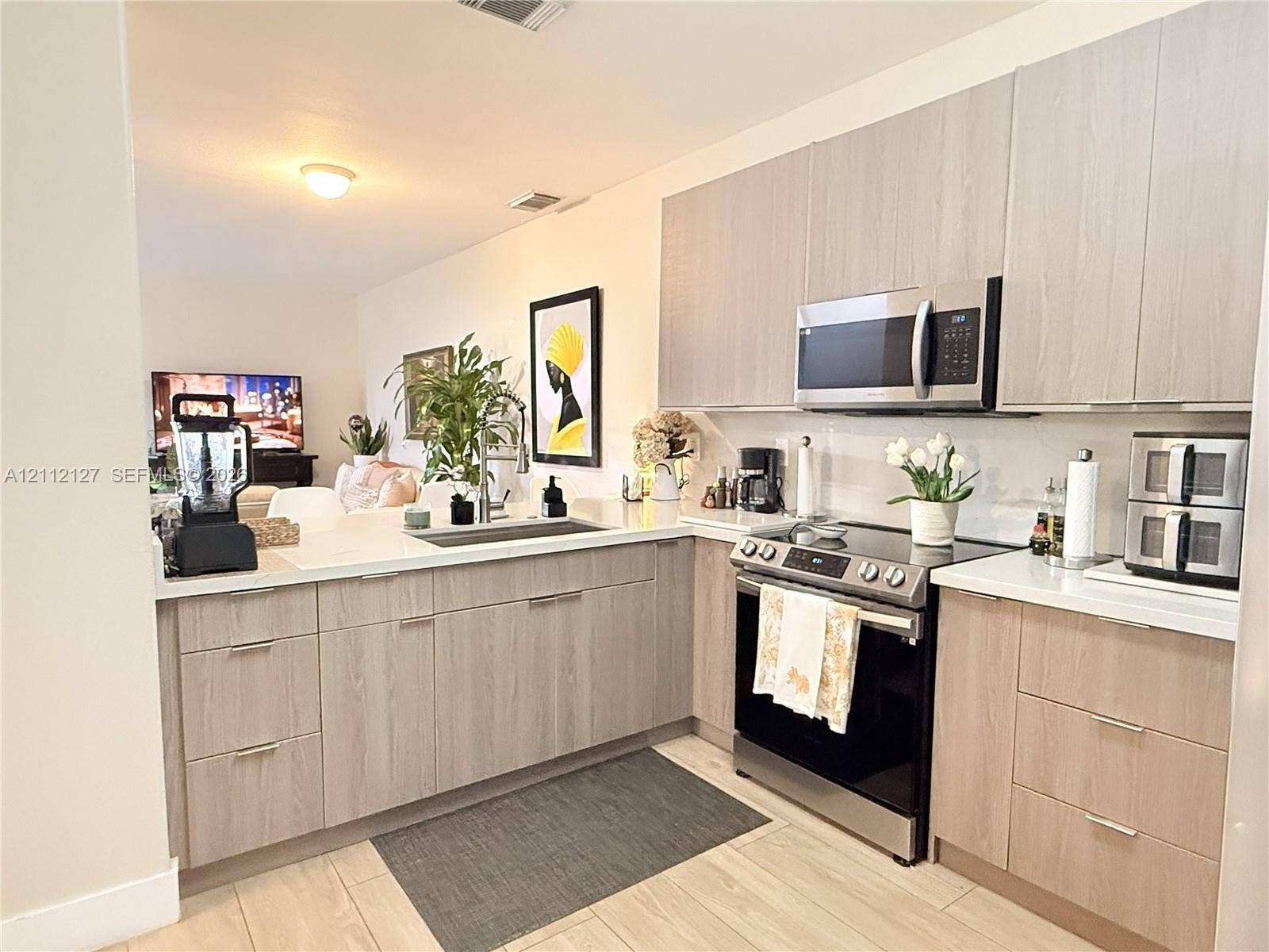 Kitchen featuring flat-panel wood-finish cabinetry, quartz countertops, stainless steel appliances, a deep undermount sink, and wood-finish flooring