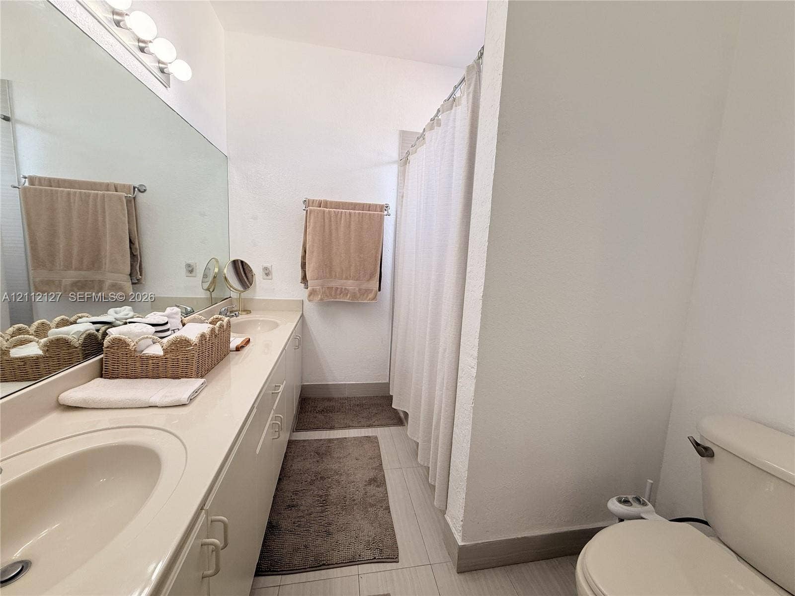 Bathroom featuring an expansive integrated vanity with dual oval sinks, a large wall-mounted mirror, and a tub-shower combination with a shower curtain