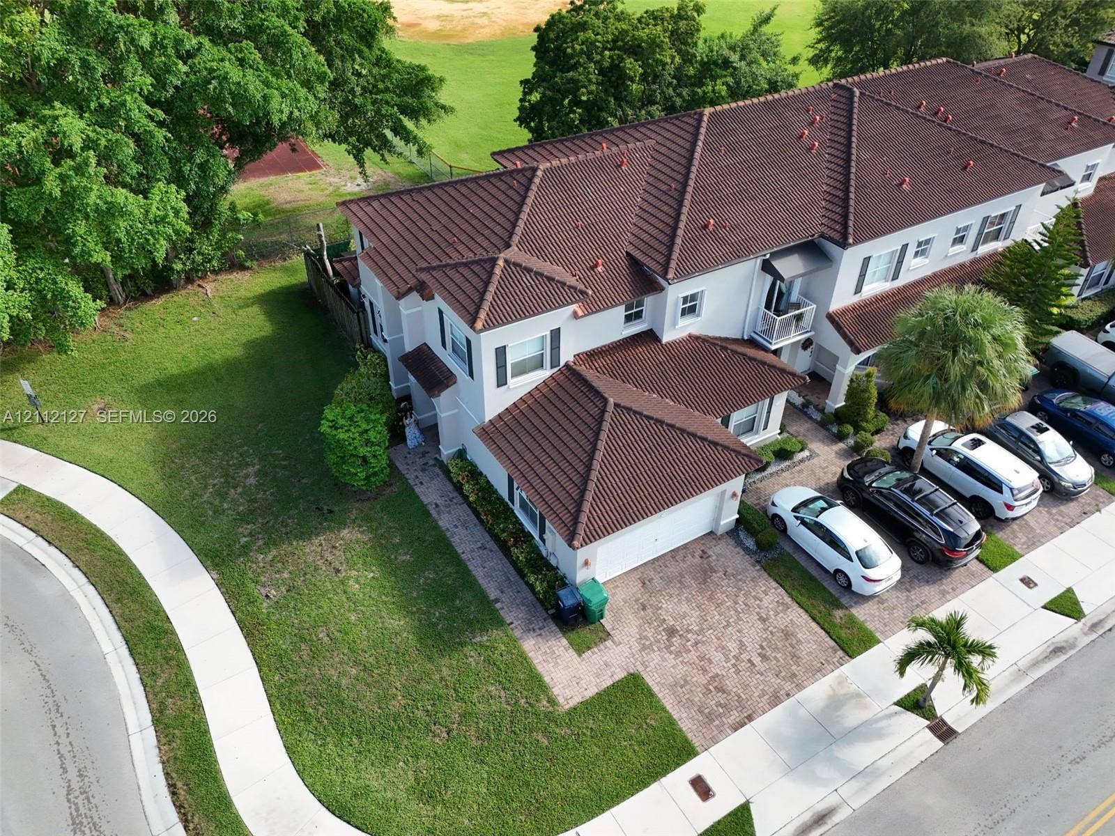 Two-story exterior featuring a tile roof, light-toned stucco facade, paved brick driveway, and a private balcony