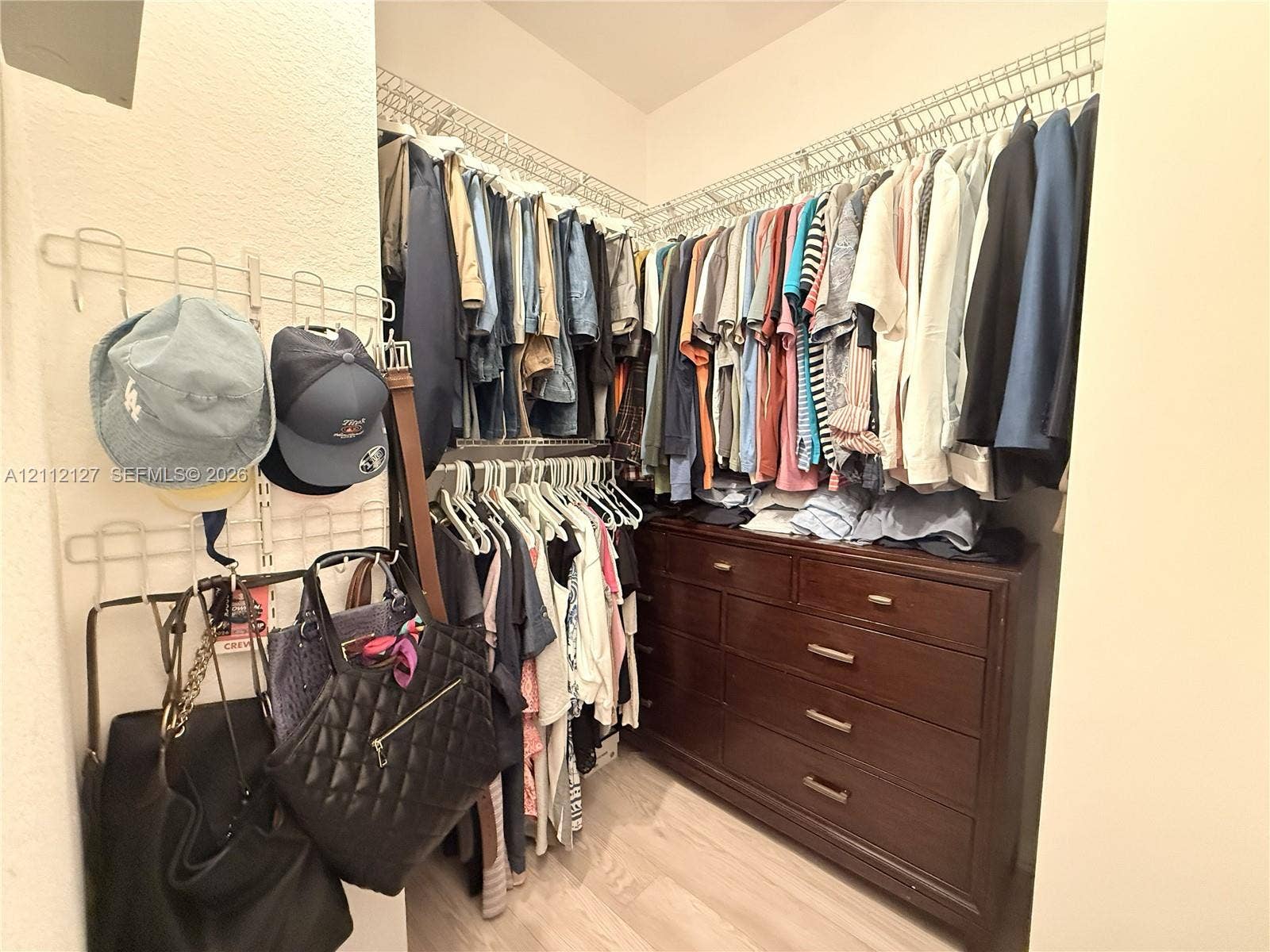 Walk-in closet featuring tiered wire shelving, wall-mounted rack storage, and wood-finish flooring