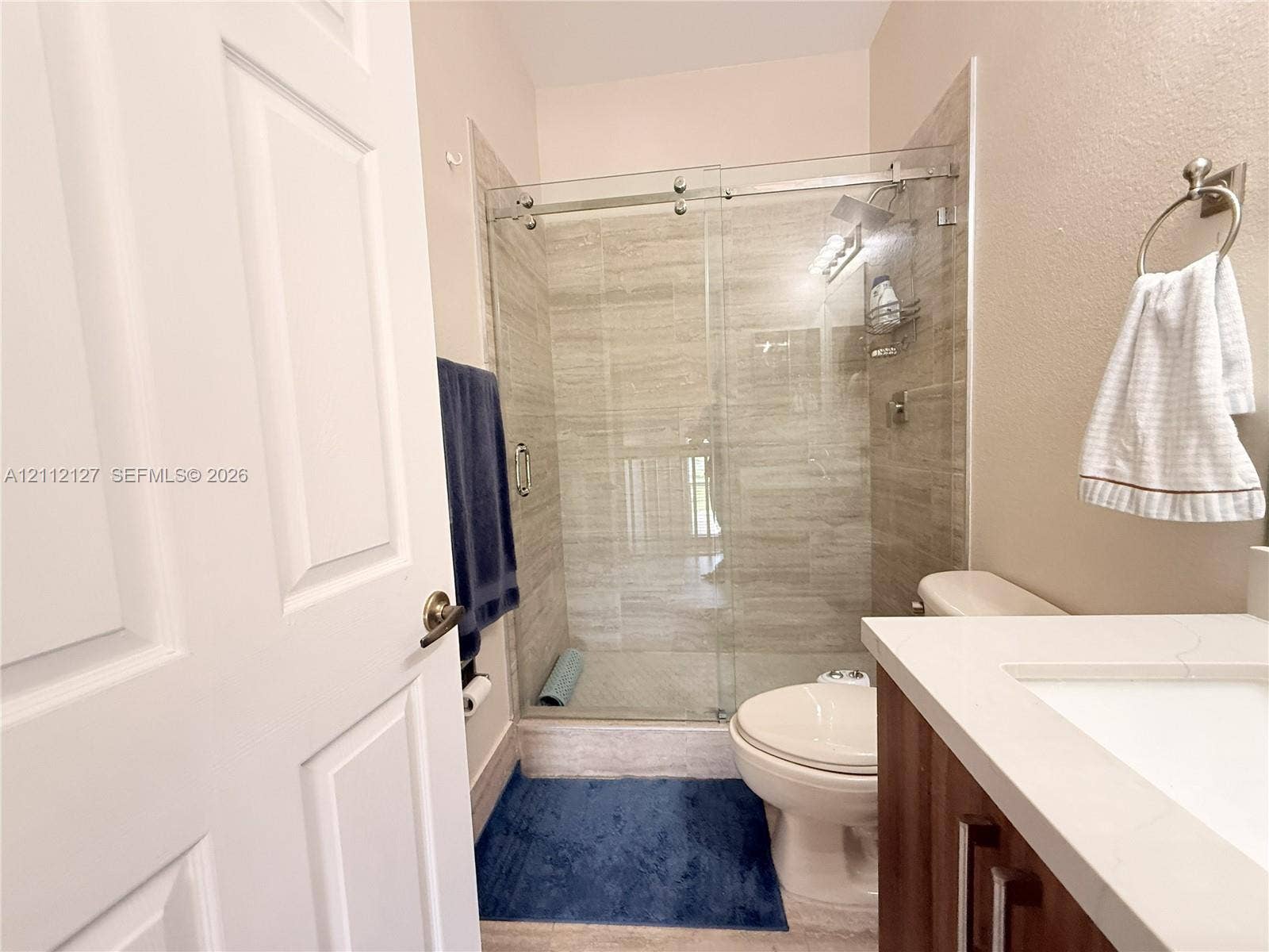 Bathroom featuring a walk-in shower with floor-to-ceiling tile surround, frameless glass sliding doors, vanity with a light-toned countertop, and integrated sink