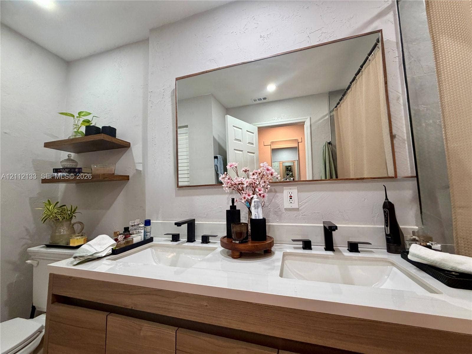 407 Bonnie Brae Way, #22, Hollywood, Hollywood, FL 33021 Dual-sink vanity with wood-finish cabinetry, white countertop, matte black widespread faucets, and two built-in wood-finish floating shelves