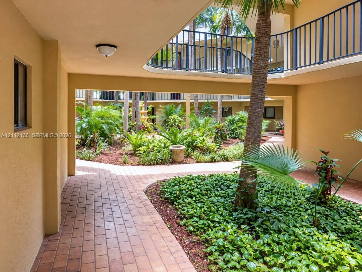 8635 NW 8th Street, #109, Miami, Miami, FL 33126 Open-air courtyard featuring brick paver walkways, lush tropical landscaping, mature palm trees, and metal railed balconies