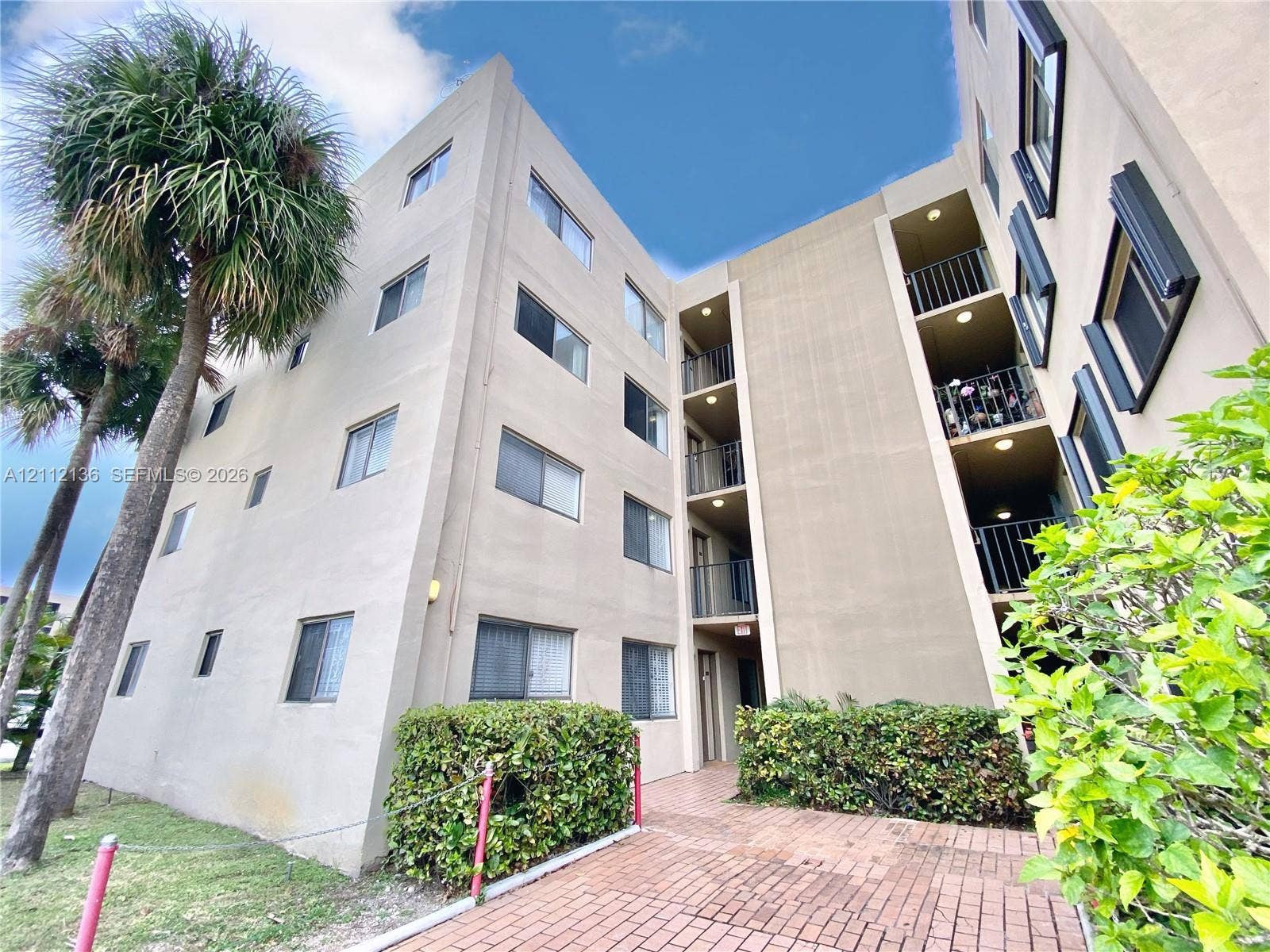 8635 NW 8th Street, #109, Miami, Miami, FL 33126 Multi-story exterior featuring a stucco facade, stacked balconies with metal railings, a brick-paved entrance path, and mature palm trees