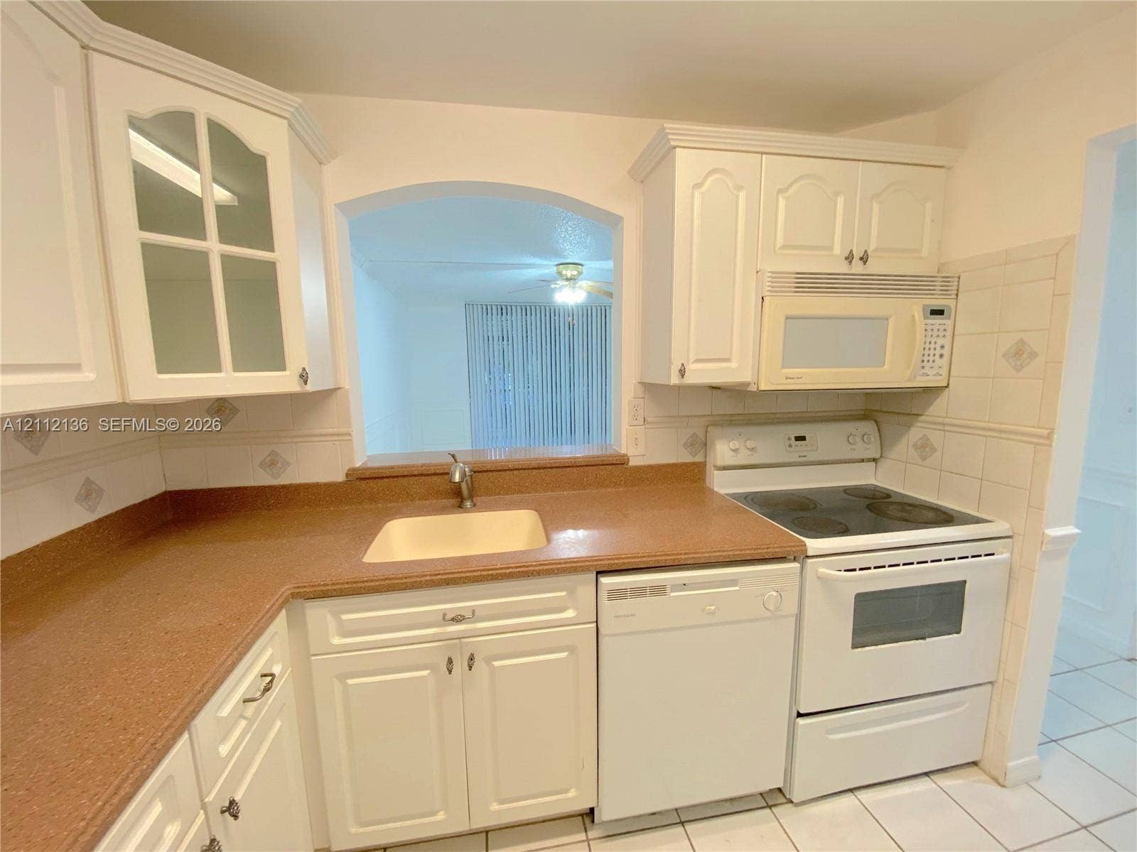 8635 NW 8th Street, #109, Miami, Miami, FL 33126 Kitchen featuring white cabinetry with glass-panel upper doors, stone-composite countertops, tile backsplash, built-in appliances, and a pass-through window