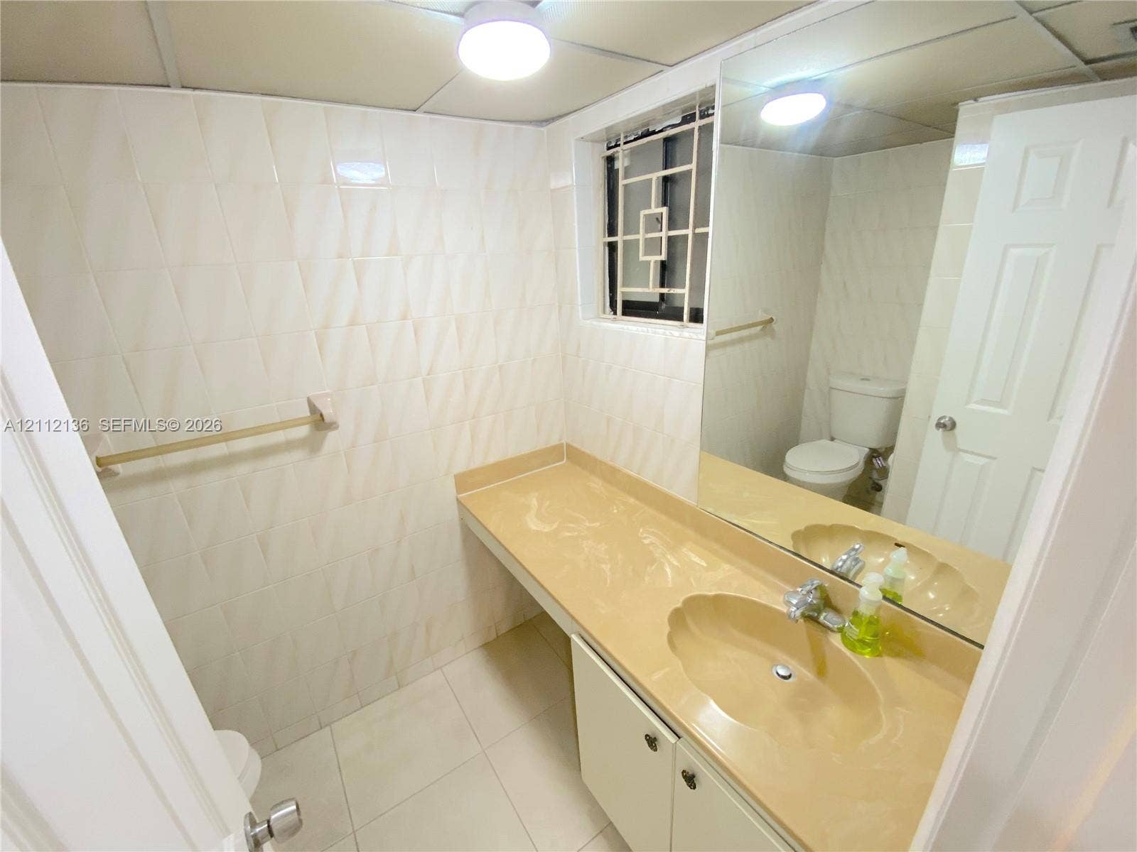 8635 NW 8th Street, #109, Miami, Miami, FL 33126 Bathroom featuring light-toned tile wall cladding, a molded vanity countertop with integrated scalloped sink, a full-width vanity mirror, and white shaker-style cabinetry