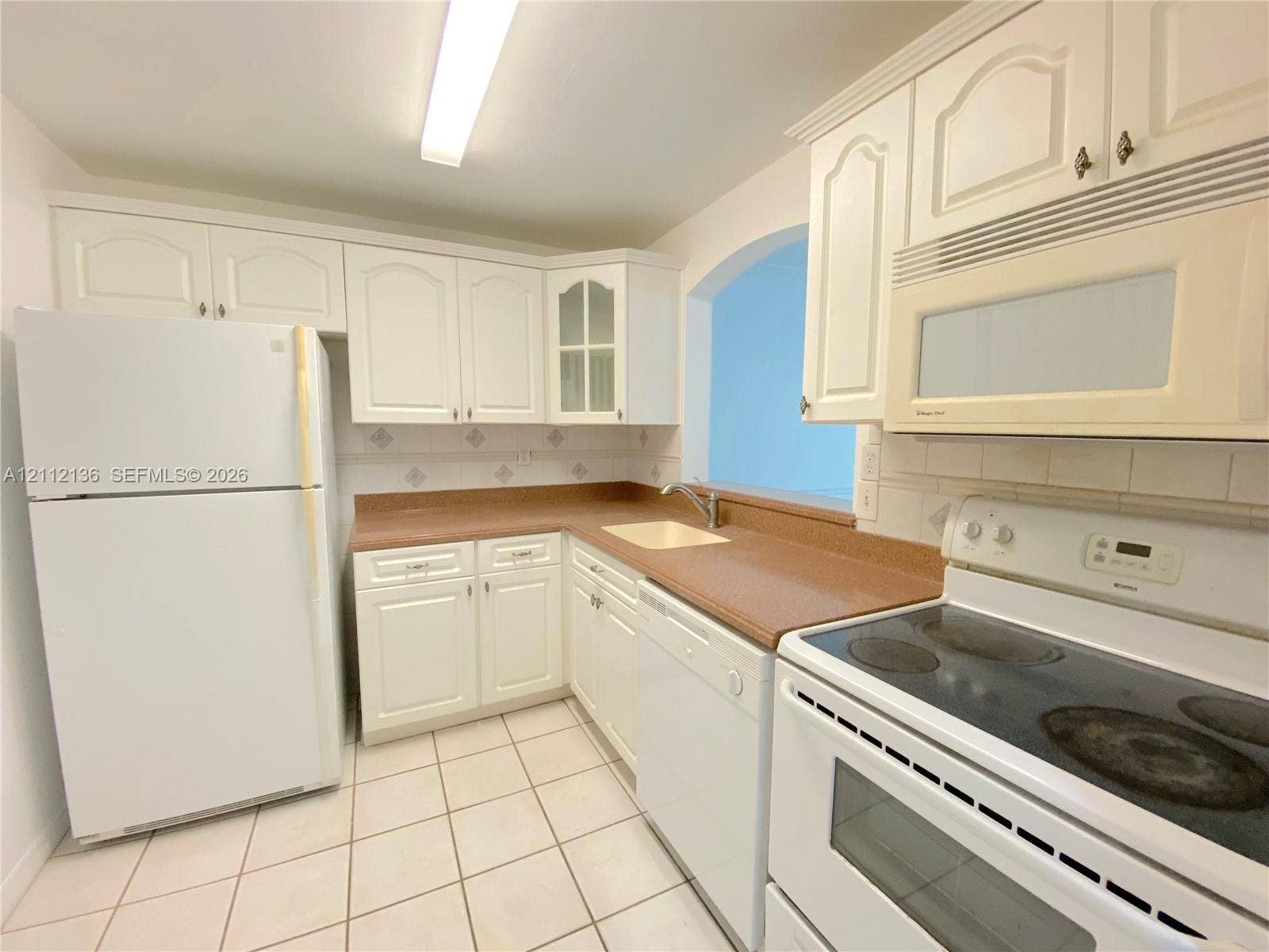 8635 NW 8th Street, #109, Miami, Miami, FL 33126 Kitchen featuring white cabinetry with glass-panel accents, solid-surface countertops, tile flooring, and integrated white appliances