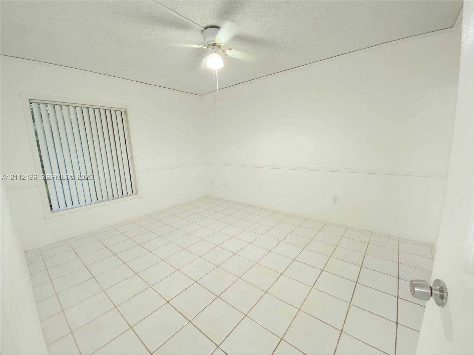 8635 NW 8th Street, #109, Miami, Miami, FL 33126 Neutral-toned room featuring large-format square tile flooring, white chair rail molding, vertical window blinds, and a central ceiling fan with an integrated light fixture
