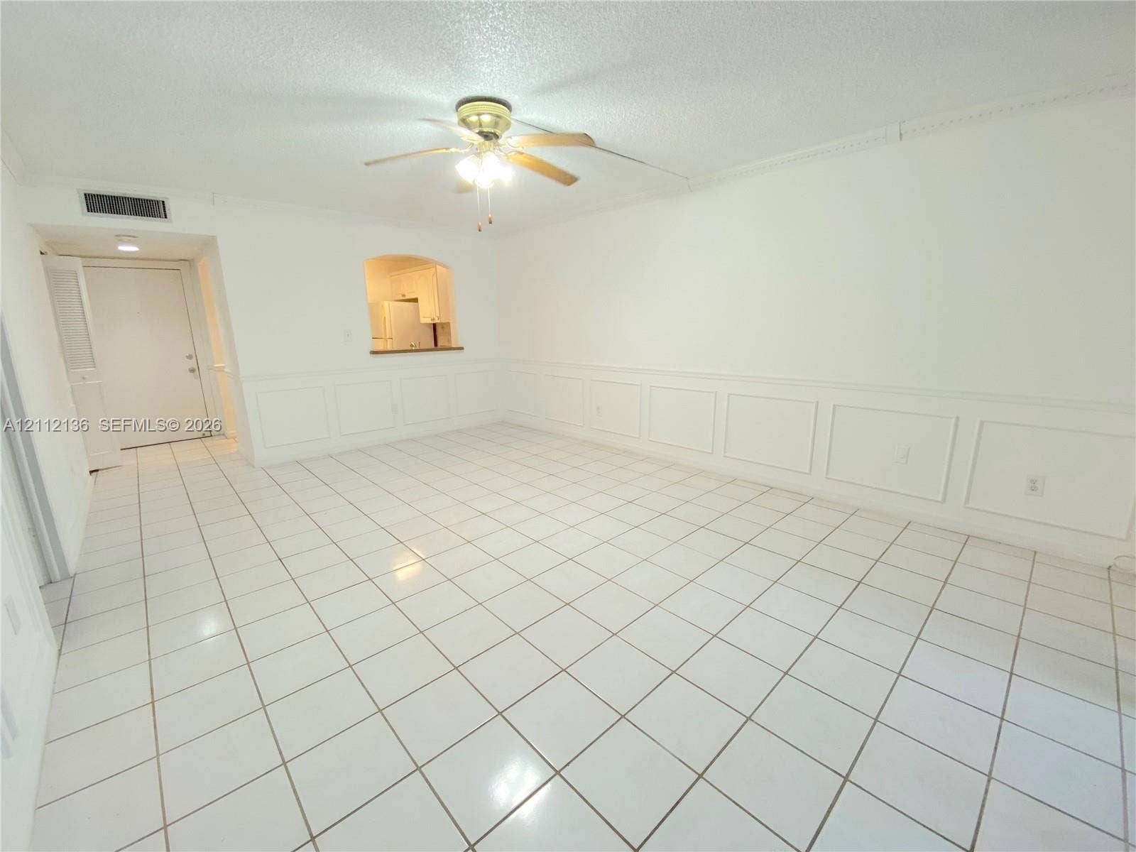 8635 NW 8th Street, #109, Miami, Miami, FL 33126 Neutral-toned interior space featuring light-colored square tile flooring, decorative wainscoting, an arched pass-through window, and a ceiling-mounted fan with integrated lighting