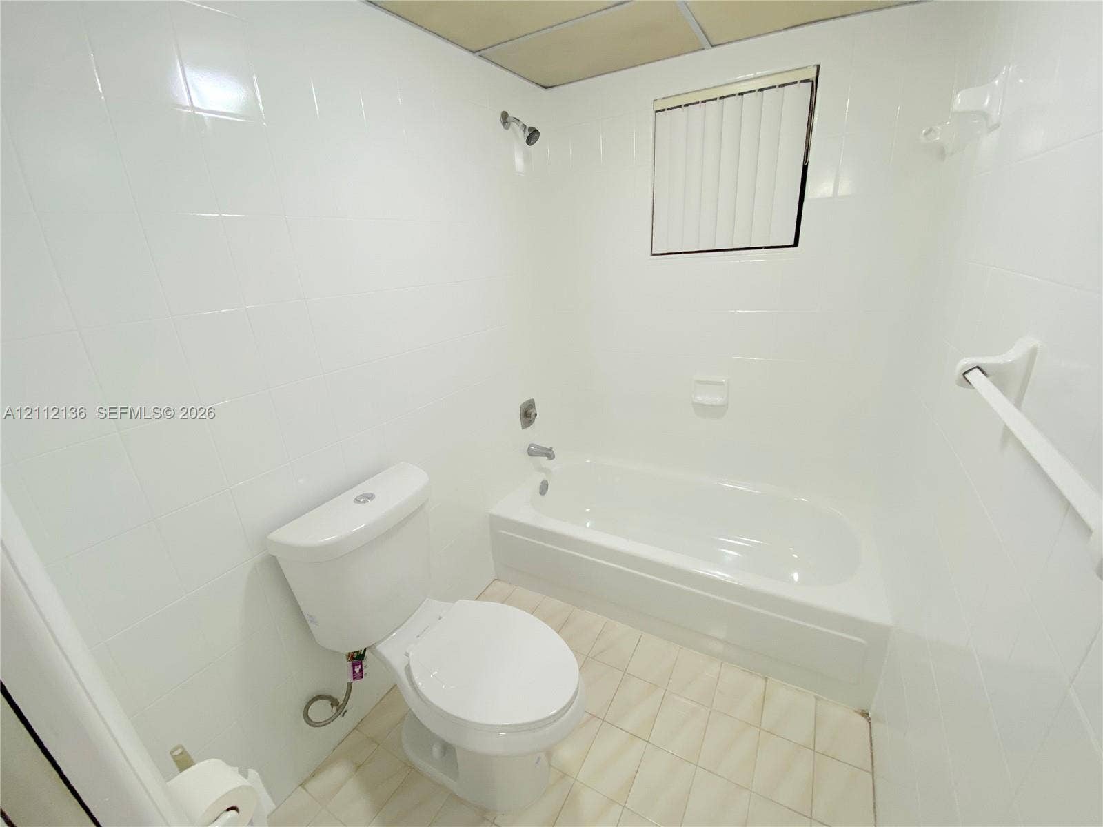 8635 NW 8th Street, #109, Miami, Miami, FL 33126 Full-height white wall tiling, porcelain bathtub with integrated shower head and diverter, porcelain toilet, and grid-pattern tile flooring