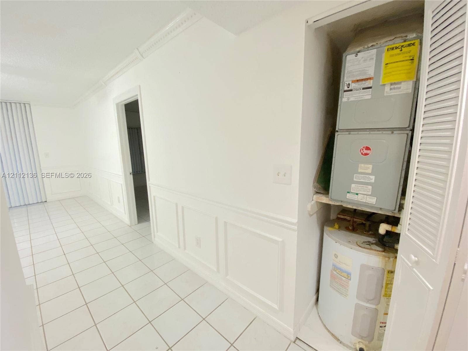 8635 NW 8th Street, #109, Miami, Miami, FL 33126 Interior space featuring white tile flooring, detailed wall wainscoting, crown molding, and a louvered-door utility closet housing the HVAC unit and water heater