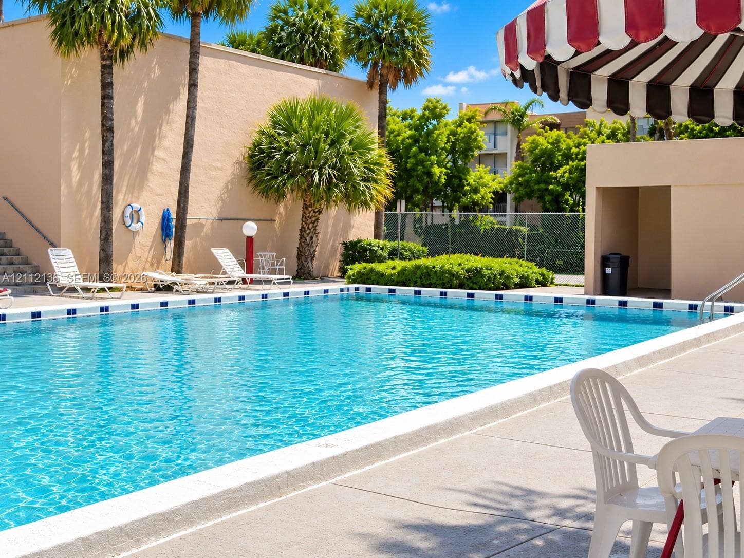 8635 NW 8th Street, #109, Miami, Miami, FL 33126 Swimming pool with a tile-bordered edge, expansive concrete deck, and mature palm trees