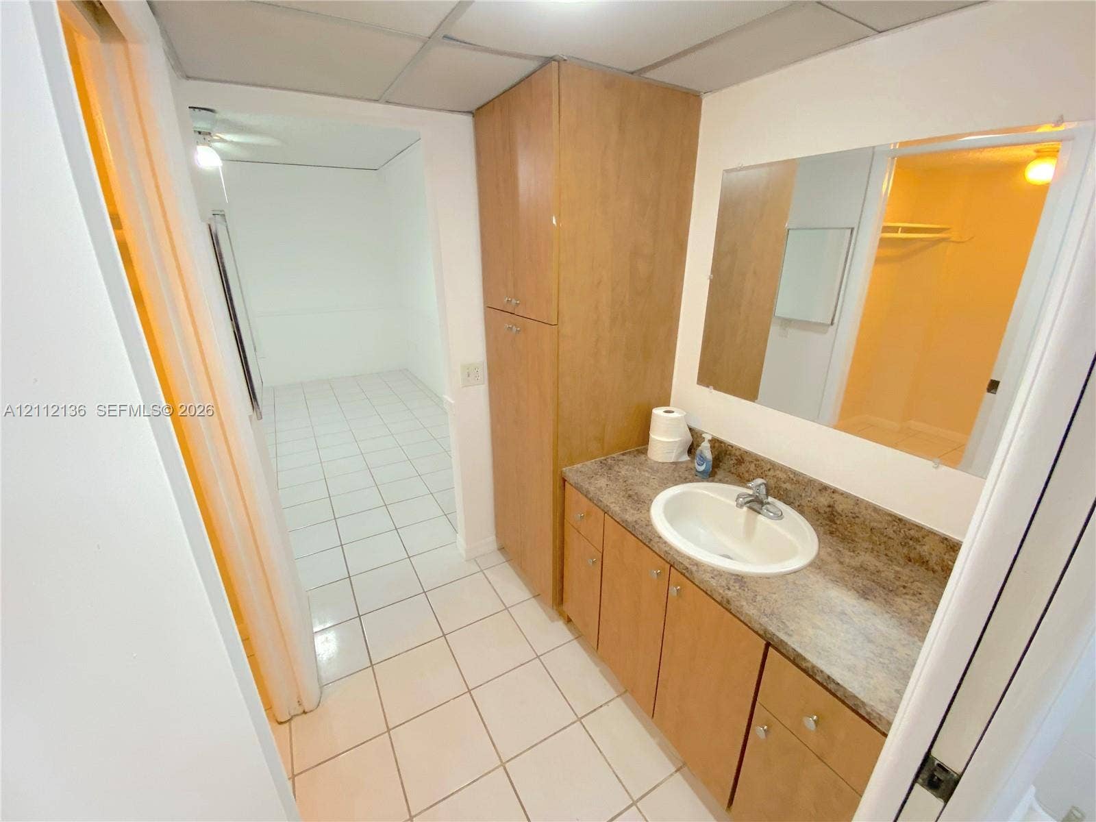 8635 NW 8th Street, #109, Miami, Miami, FL 33126 Vanity featuring wood-finish cabinetry, a full-height storage cabinet, a solid-surface countertop, and a recessed oval sink