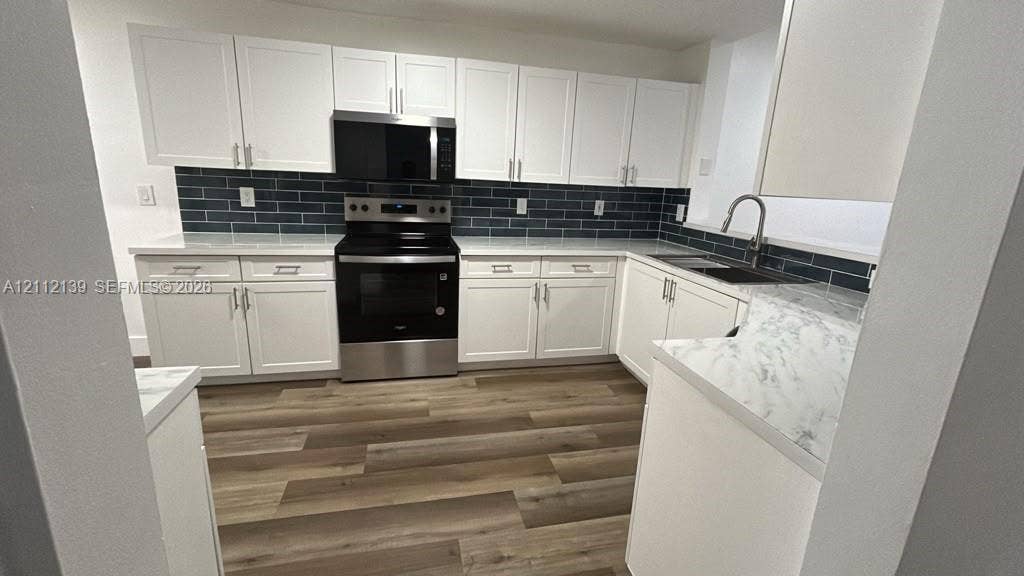 Kitchen featuring white shaker-style cabinetry, stainless steel appliances, dark subway tile backsplash, stone-finish countertops, and wood-finish flooring