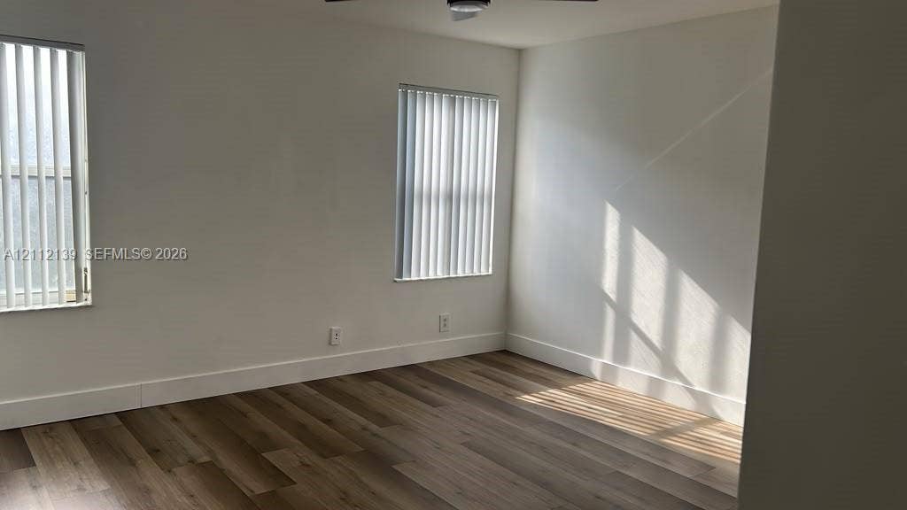 Neutral interior space featuring wood-finish flooring, white walls, and vertical window blinds