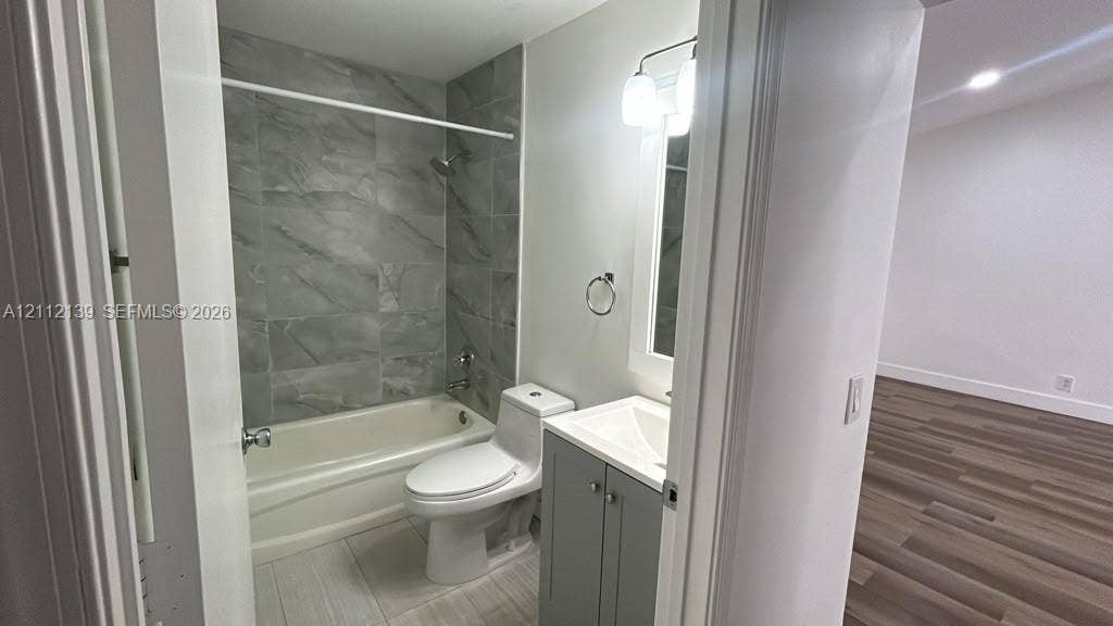 Bathroom featuring a gray vanity cabinet with a white integrated sink, porcelain tile tub surround with a metallic shower fixture, and light-toned tile flooring