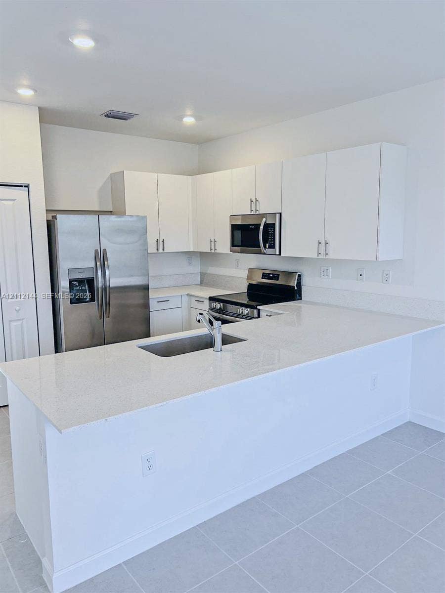 29216 SW 163rd Court, #29216, Homestead, Homestead, FL 33033 Kitchen featuring white cabinetry, solid-surface countertops, a stainless steel refrigerator, a built-in microwave, and tile flooring
