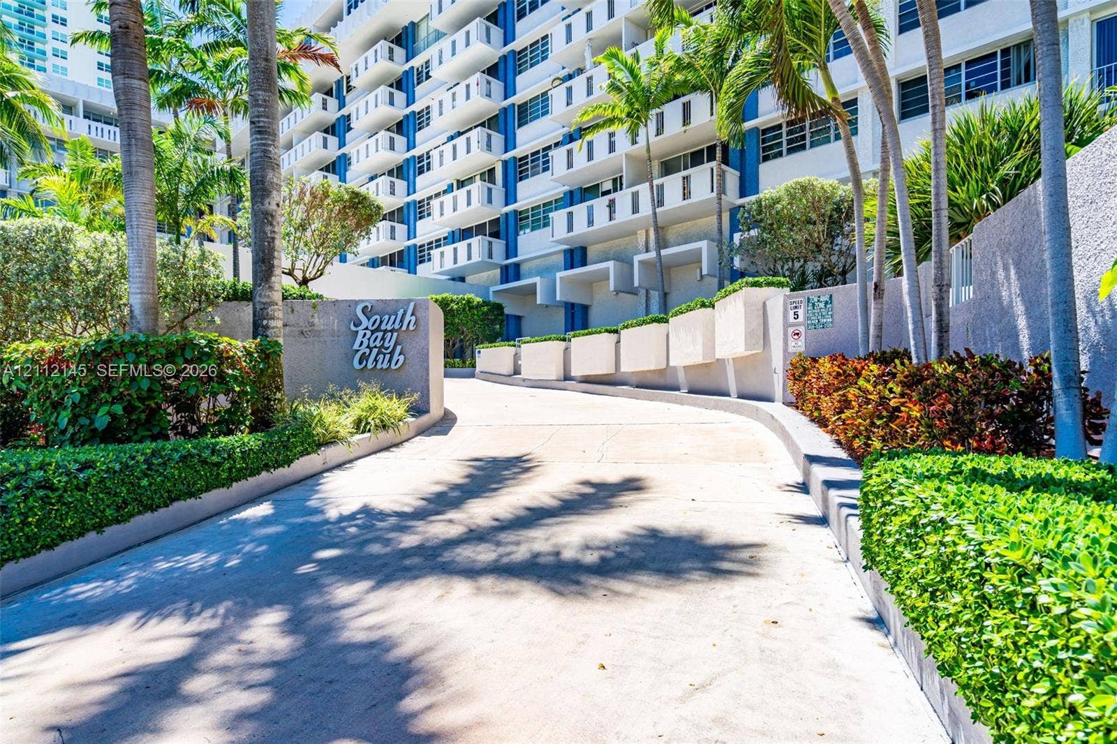 800 West Avenue, #PH-37, Miami Beach, FL 33139 Concrete driveway entrance featuring tropical landscaping, manicured hedges, and multi-story building facade with private balconies