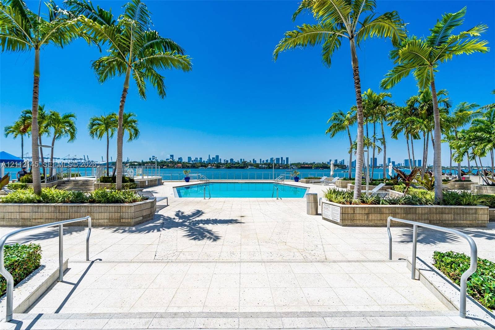 800 West Avenue, #PH-37, Miami Beach, FL 33139 Outdoor pool featuring a paved deck, tiered stone planters, mature palm trees, and waterfront perimeter fencing