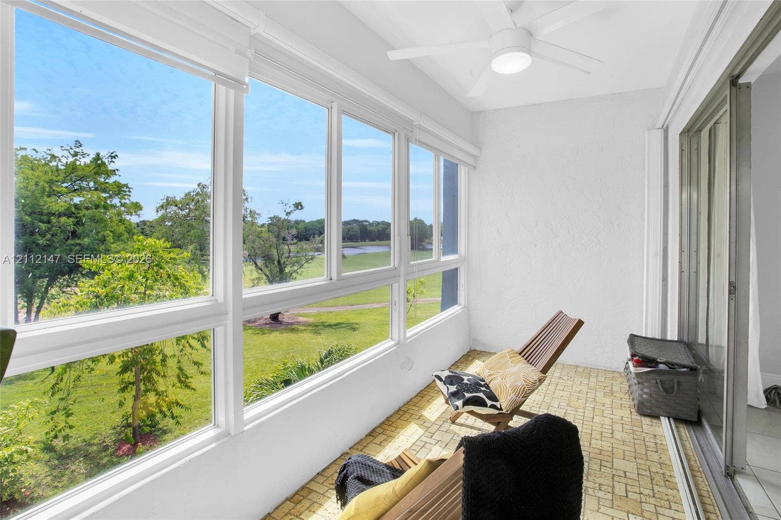 8331 Sands Point Boulevard, #C308, Tamarac, FL 33321 Enclosed sunroom featuring expansive windows, brick-patterned flooring, a ceiling-mounted light fixture, and textured wall finishes