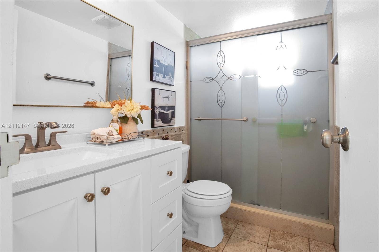 8331 Sands Point Boulevard, #C308, Tamarac, FL 33321 White vanity with a solid-surface countertop and dual-handle faucet, integrated rectangular sink, wall-mounted mirror, and a walk-in shower featuring an etched glass enclosure