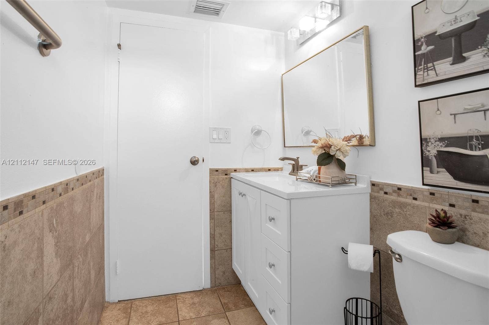 8331 Sands Point Boulevard, #C308, Tamarac, FL 33321 Bathroom featuring a white vanity cabinet with drawers, a rectangular mirror with a metallic frame, neutral-toned wall and floor tile, and a three-light fixture