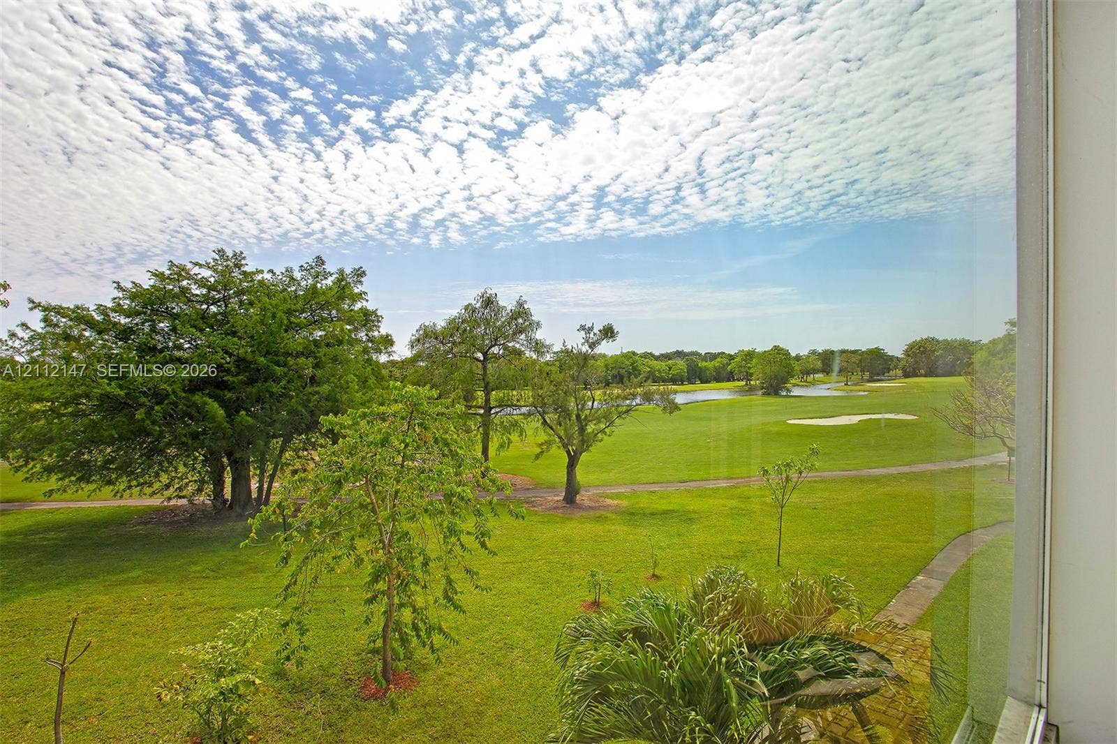 8331 Sands Point Boulevard, #C308, Tamarac, FL 33321 Full-height window pane providing exterior visibility of a landscaped lawn, mature trees, a water feature, and a golf course green