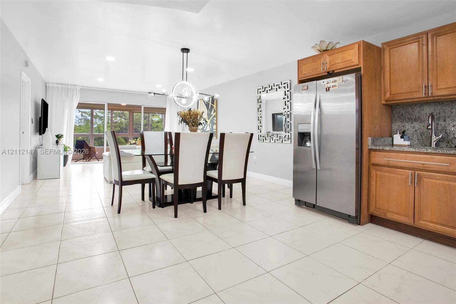 8331 Sands Point Boulevard, #C308, Tamarac, FL 33321 Kitchen area featuring natural wood cabinetry, stone countertops, a stainless steel refrigerator, and large-format tile flooring