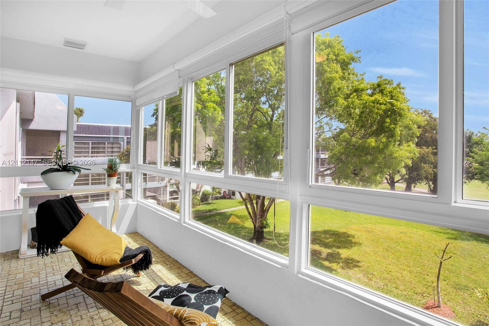 8331 Sands Point Boulevard, #C308, Tamarac, FL 33321 Enclosed sunroom featuring expansive window walls, white-framed glass sliders, and textured stone-finish flooring