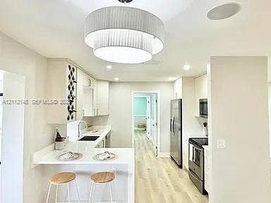 1753 N 16th Court N, Lake Worth, Lake Worth, FL 33460 Kitchen featuring tiered pendant lighting, light wood-finish flooring, white cabinetry with built-in wine storage, stone countertops, and stainless steel appliances