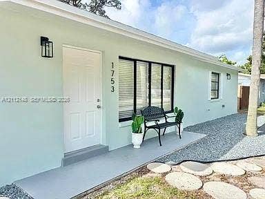 1753 N 16th Court N, Lake Worth, Lake Worth, FL 33460 Exterior facade featuring light-toned smooth stucco, a solid entry door with matte black lantern-style sconce, large picture windows with black frames, and a concrete front entry landing