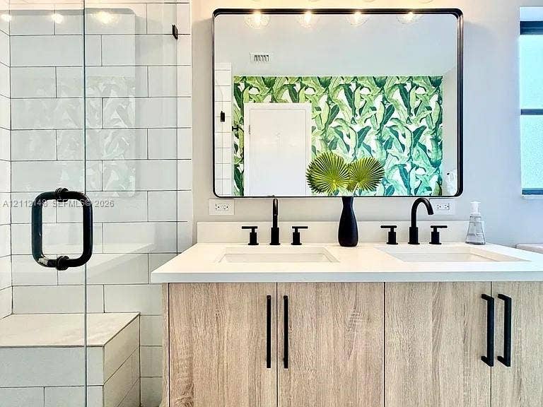 1753 N 16th Court N, Lake Worth, Lake Worth, FL 33460 Dual-sink vanity with light-tone wood-finish cabinetry, white countertop, rectangular undermount sinks, and matte black fixtures, paired with a walk-in shower featuring subway tile surrounds and a glass enclosure