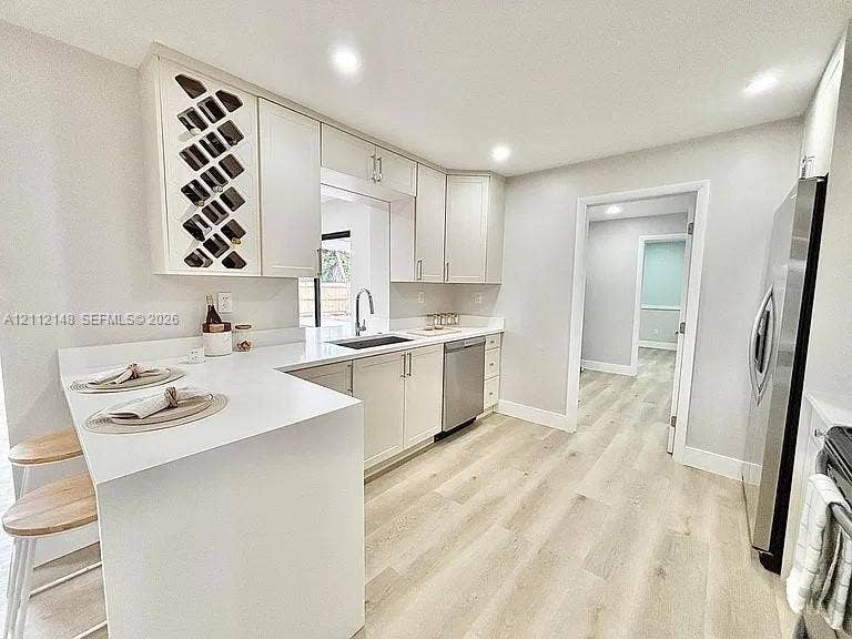 1753 N 16th Court N, Lake Worth, Lake Worth, FL 33460 Kitchen featuring white Shaker-style cabinetry with integrated wine rack, solid-surface countertops, stainless steel appliances, and wood-finish flooring