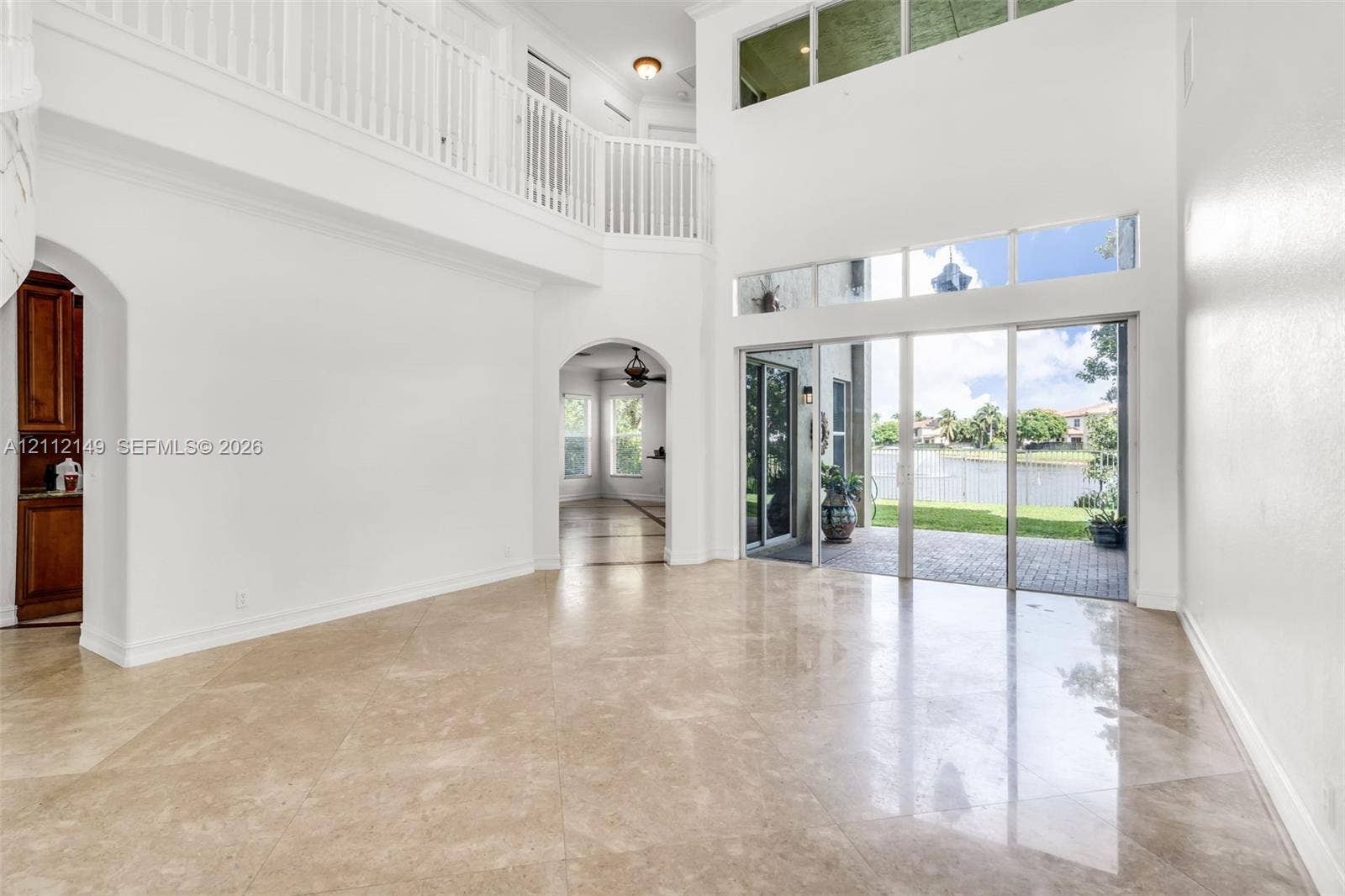 Double-height ceiling, arched architectural openings, polished stone flooring, second-level railed landing, and floor-to-ceiling glass sliding doors