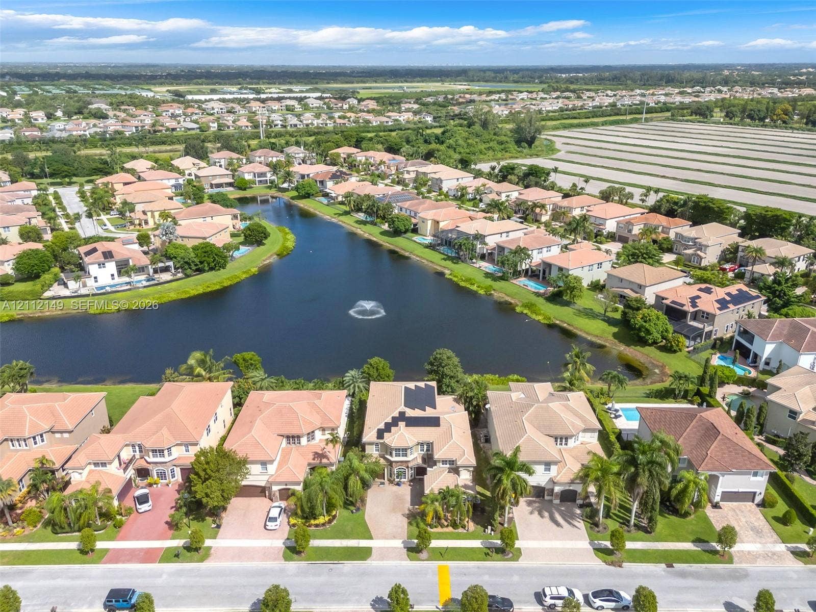 Aerial perspective of a residential community featuring multi-story homes with tile roofs, paved driveways, waterfront access to a central lake, and integrated solar panel installations