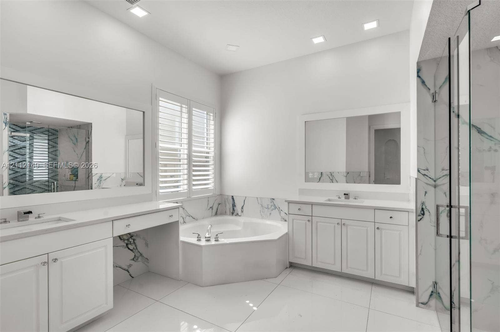 Bathroom featuring white cabinetry, integrated vanity, dual-basin sinks, jetted soaking tub, and stone-accented shower enclosure with glass door