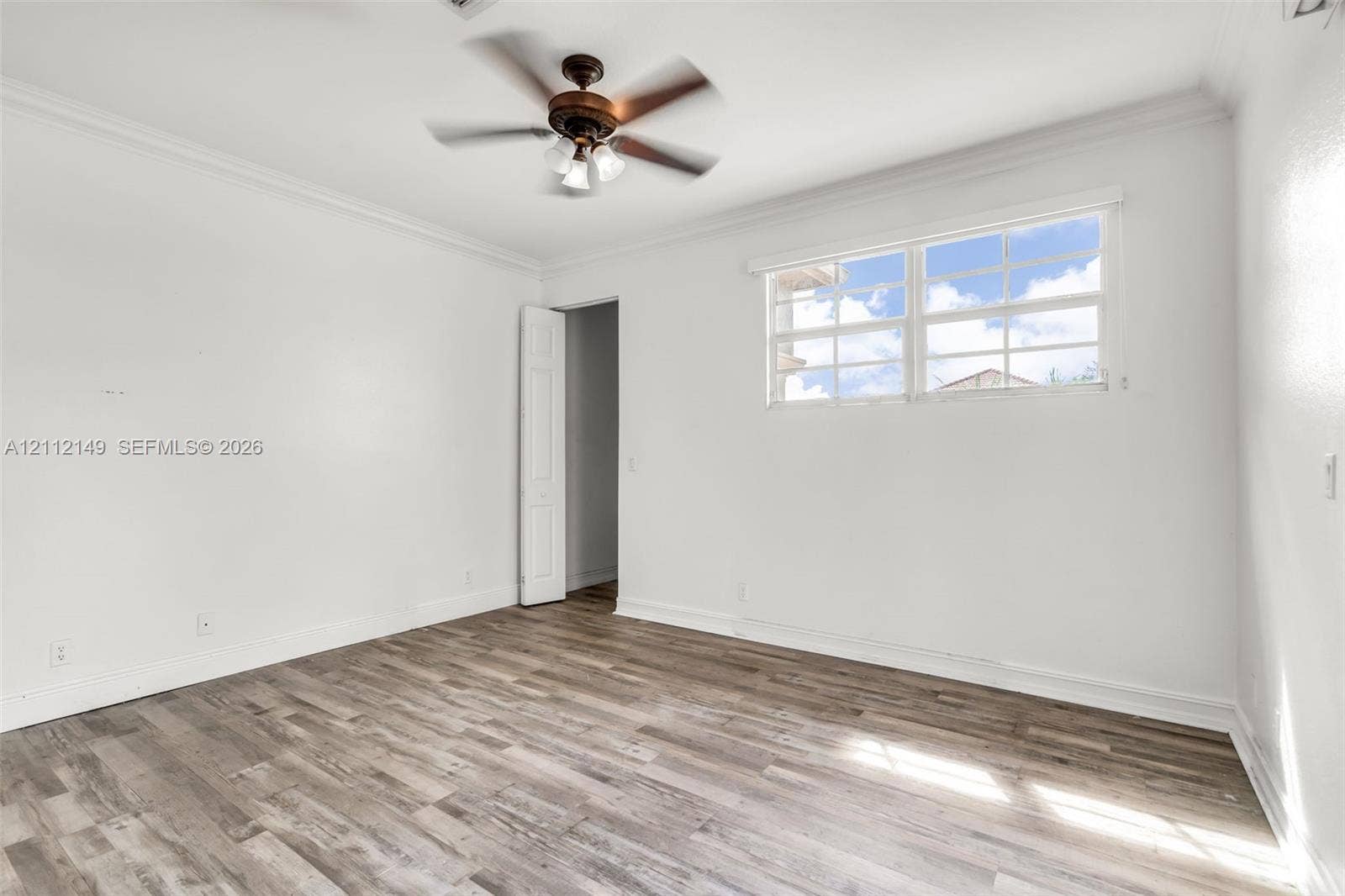 Wood-finish flooring, multi-pane window, ceiling fan with integrated lighting, and crown molding