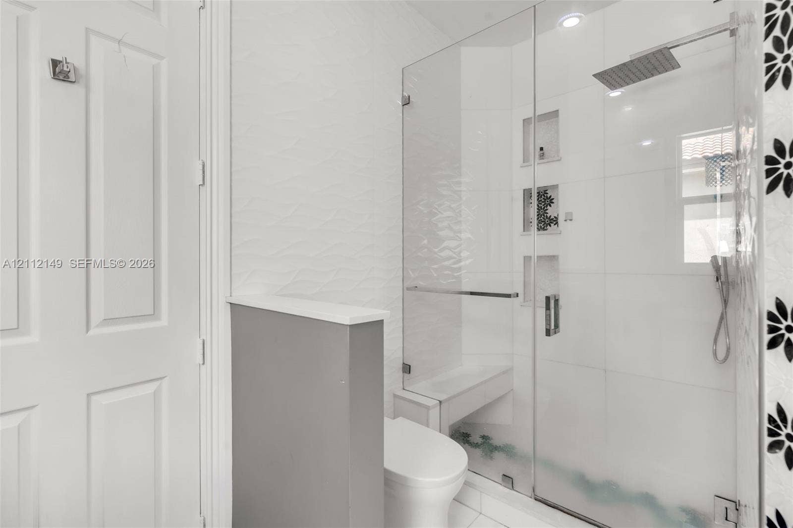Walk-in shower featuring a glass enclosure, square rainfall shower head, handheld sprayer, built-in bench, and recessed wall niches