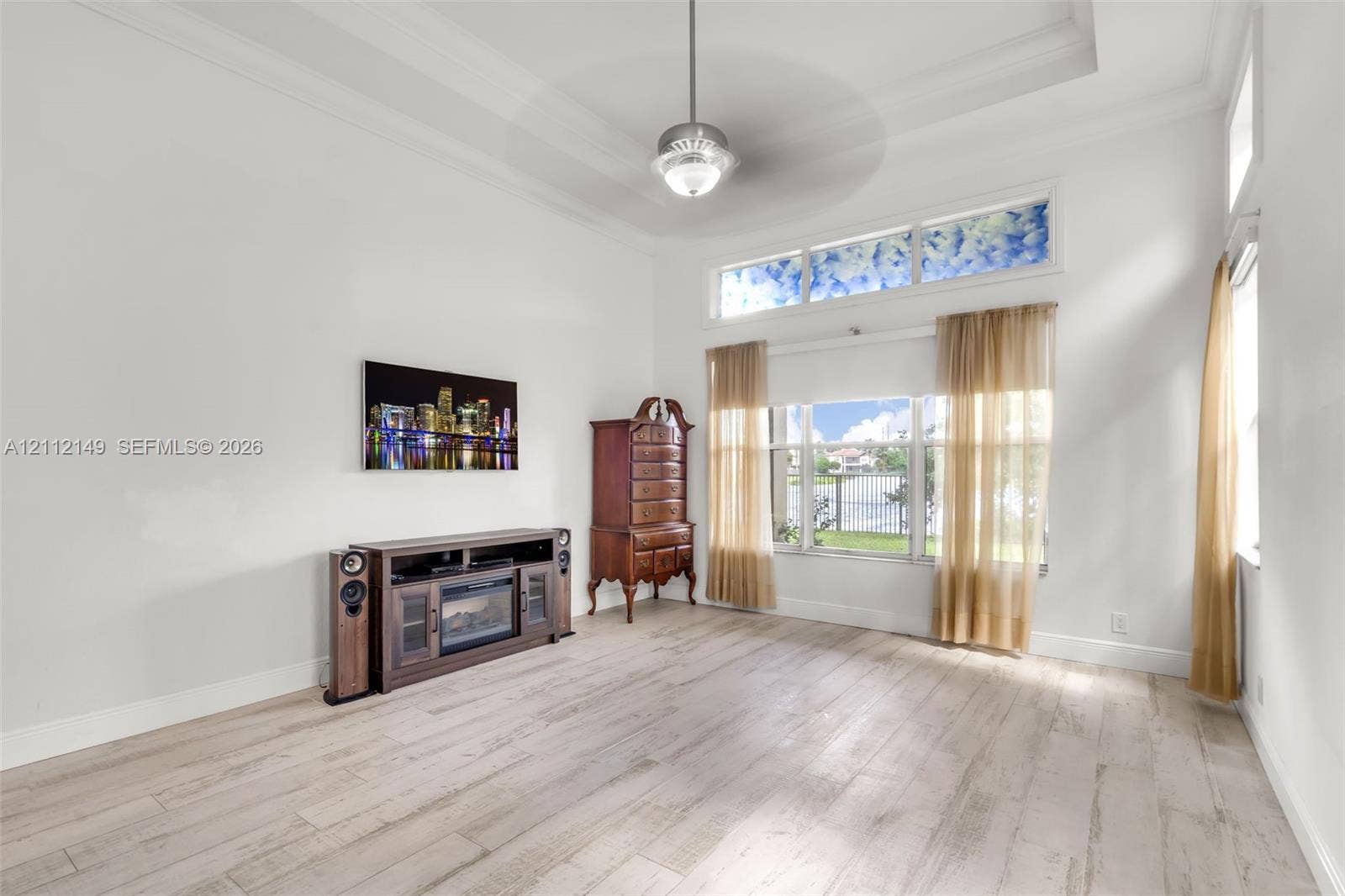 High-ceiling room featuring wood-finish flooring, a tray ceiling with a central ceiling fan, and large windows with a transom above