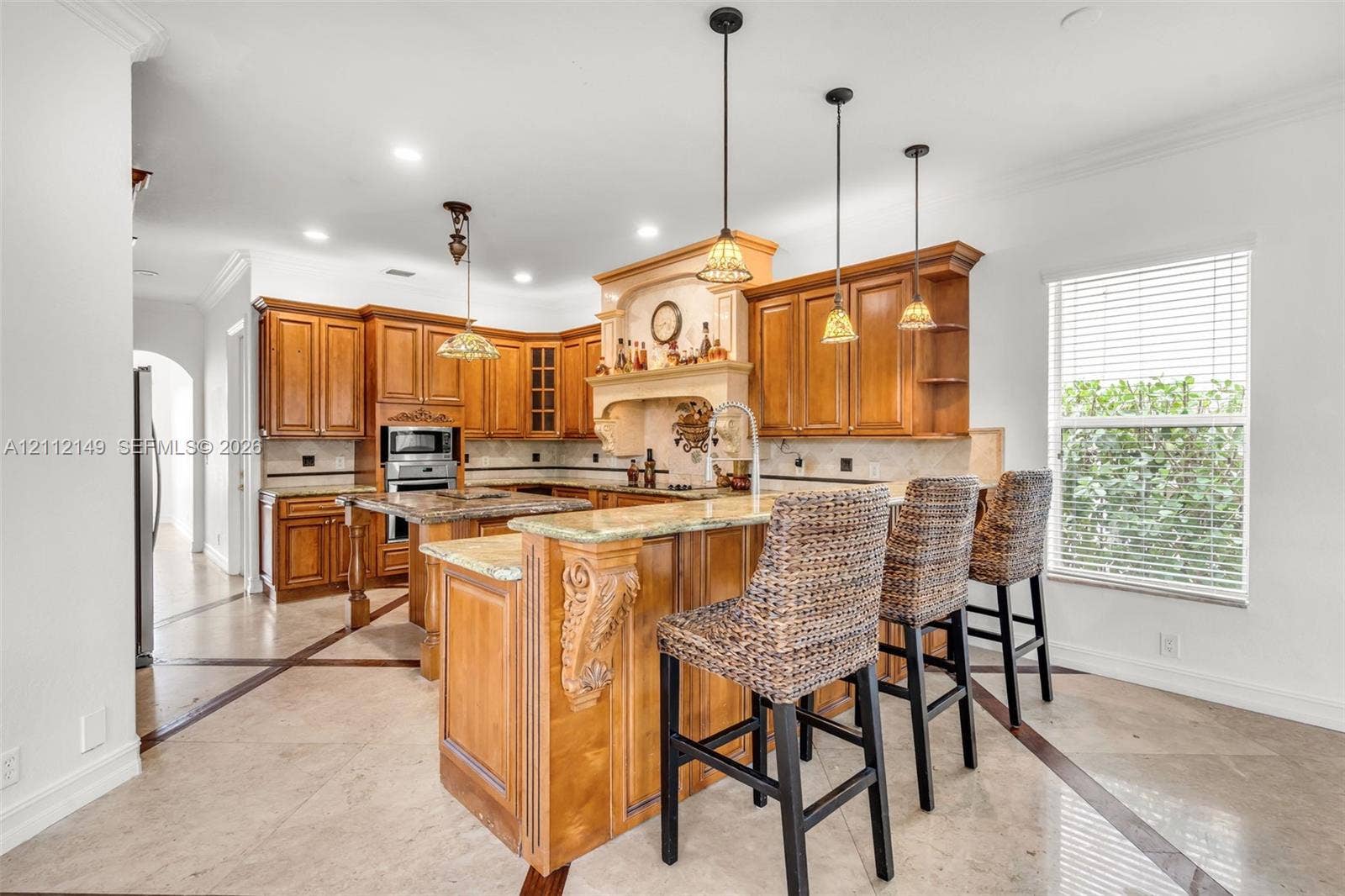 Kitchen featuring wood cabinetry, stone countertops, a tiered breakfast bar with corbel detailing, built-in stainless steel appliances, and tile flooring with decorative inlay