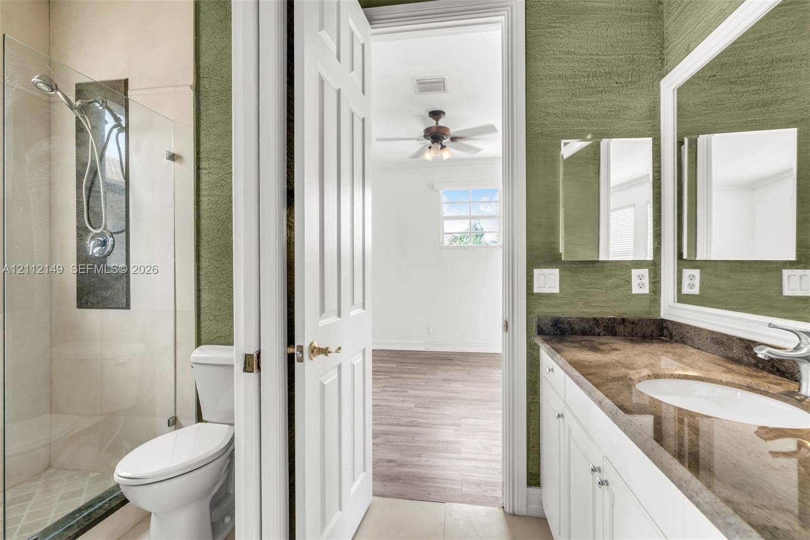 Bathroom featuring a walk-in glass-enclosed shower with metallic hardware, white cabinetry, a stone-finish countertop with an integrated basin, and textured green wall finishes
