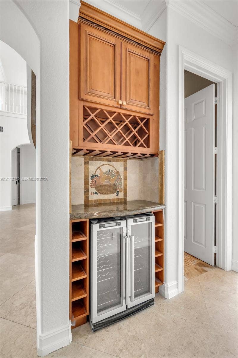 Built-in cabinetry featuring wood-finish wine storage, glass-door beverage refrigeration, a stone-surfaced countertop, and decorative mosaic tile backsplash