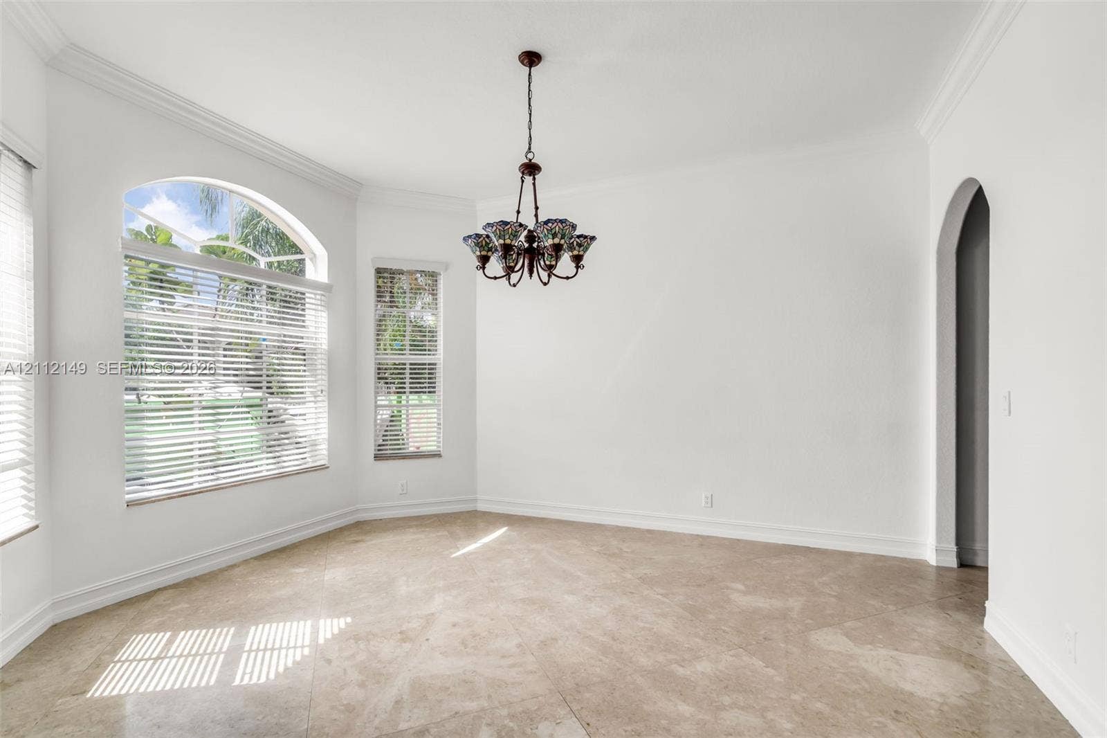 Room featuring arched windows, stone-finish flooring, a multi-arm chandelier, crown molding, and an arched entryway