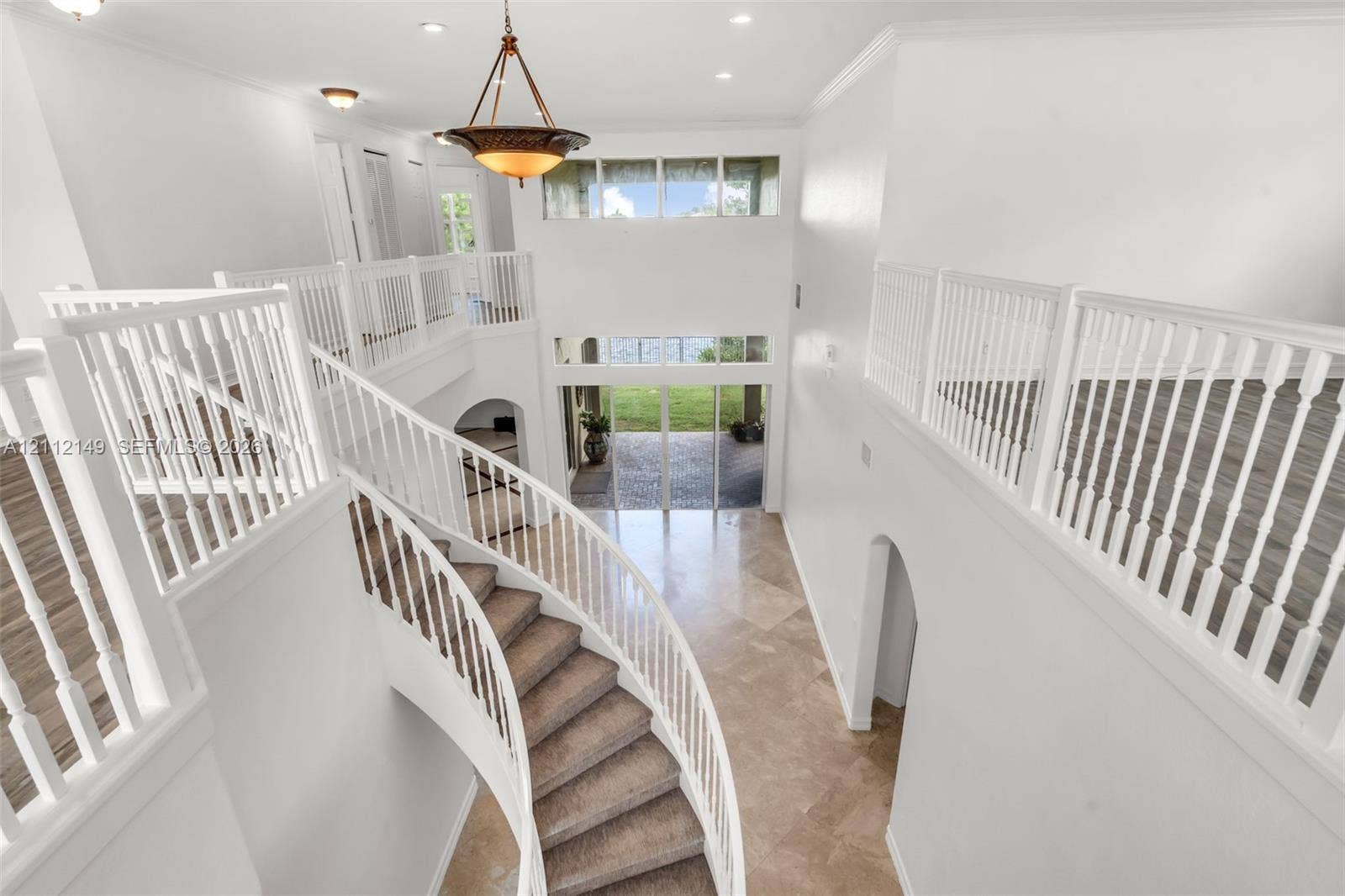 Grand foyer featuring a curved staircase, stone tile flooring, multi-level ceiling heights, white wood railings, and a tiered chandelier