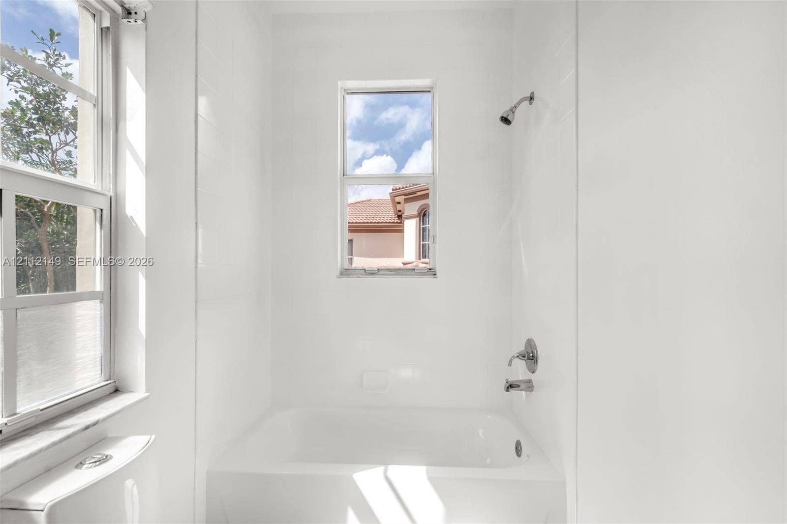Bathtub and shower combination featuring full-height white wall tile, dual windows, and polished chrome plumbing fixtures