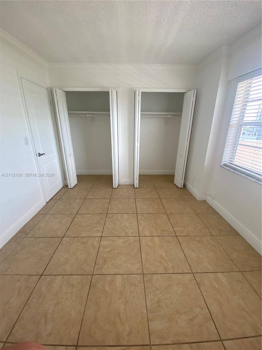 Room featuring large-format tile flooring, two closets with bi-fold doors, and a window with horizontal blinds