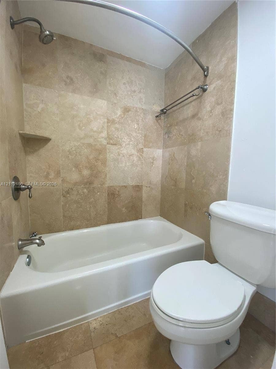 Neutral-toned tile flooring throughout the interior space, featuring a vanity with wood-finish cabinetry, a stone-surface countertop, and a wall-mounted vanity mirror with integrated lighting